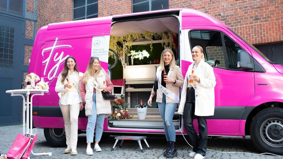 Four women holding drinks by pink van.