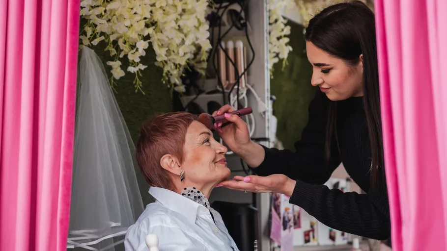Makeup artist applying makeup to a seated woman.