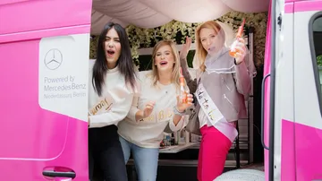 Drei Frauen feiern in einem rosa Van.