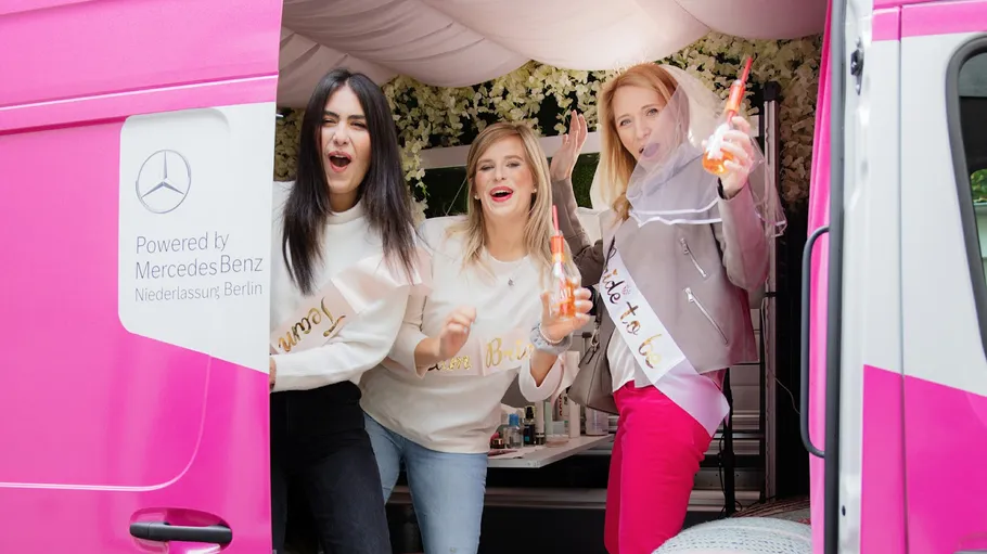 Drei Frauen feiern in einem rosa Van.