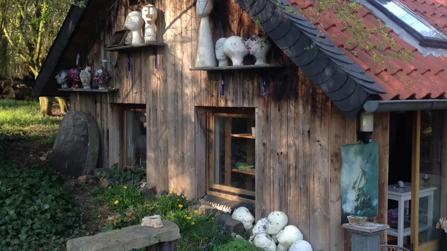 Wooden cabin with sculptures outside in garden.