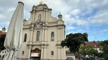Barocke Kirchenfassade mit bewölktem Himmel.