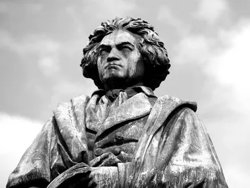 Statue of a composer standing majestically under cloudy sky.