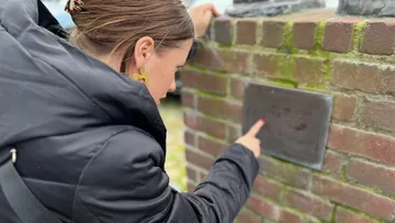 Frau liest Tafel an Ziegelmauer im Freien.