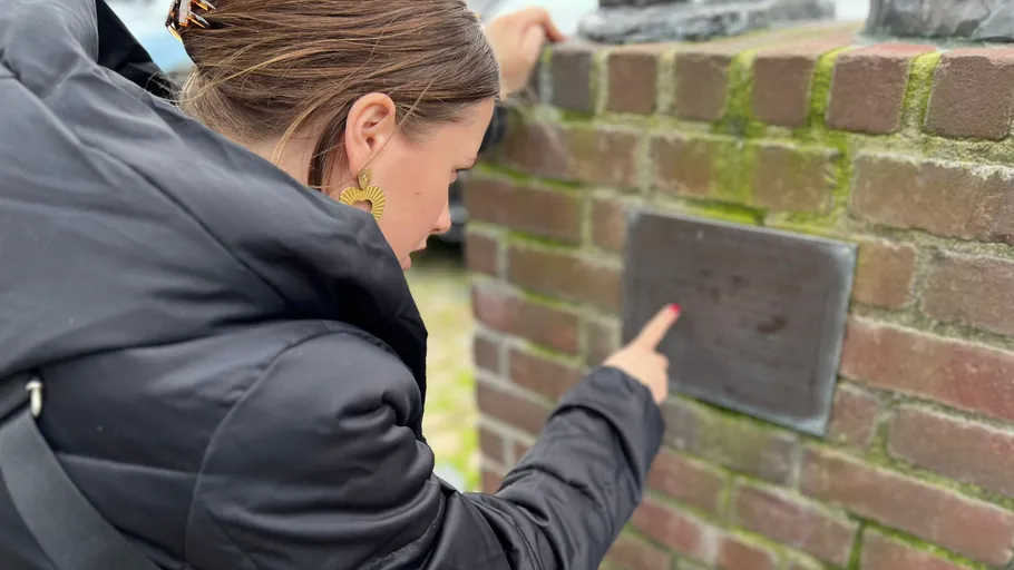 Frau liest Tafel an Ziegelmauer im Freien.