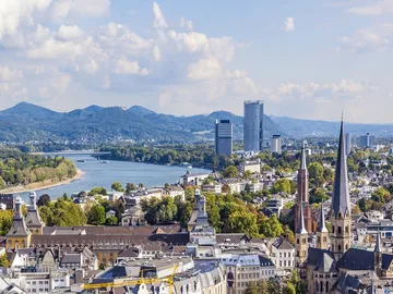 Stadtansicht mit Fluss, Gebäuden und Bergen im Hintergrund.
