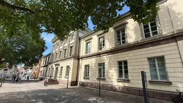 Historisches Gebäude an baumgesäumter Straße.