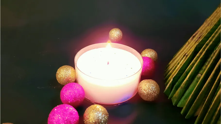 Candle surrounded by glitter balls, festive setting.