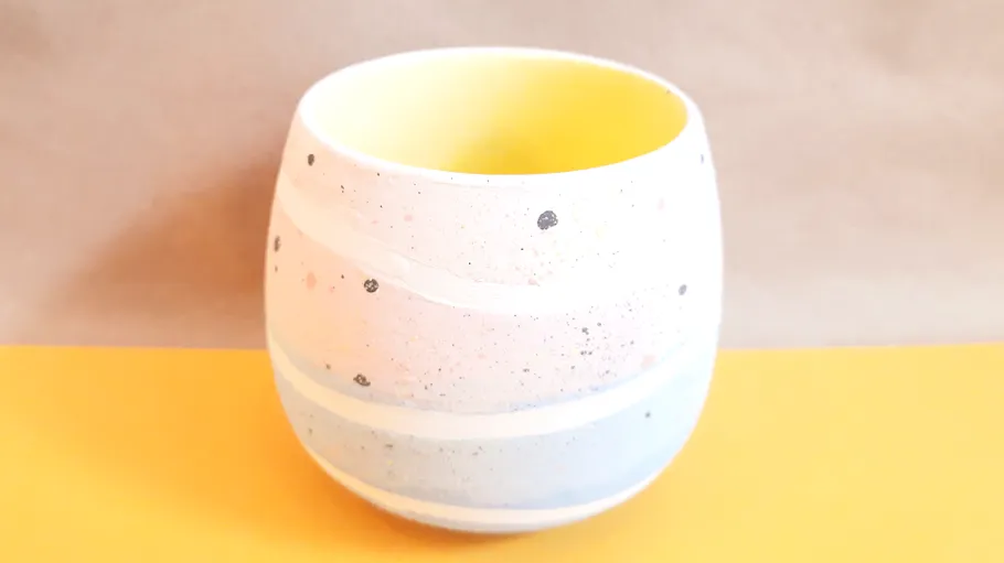 Speckled ceramic planter with yellow interior on table.