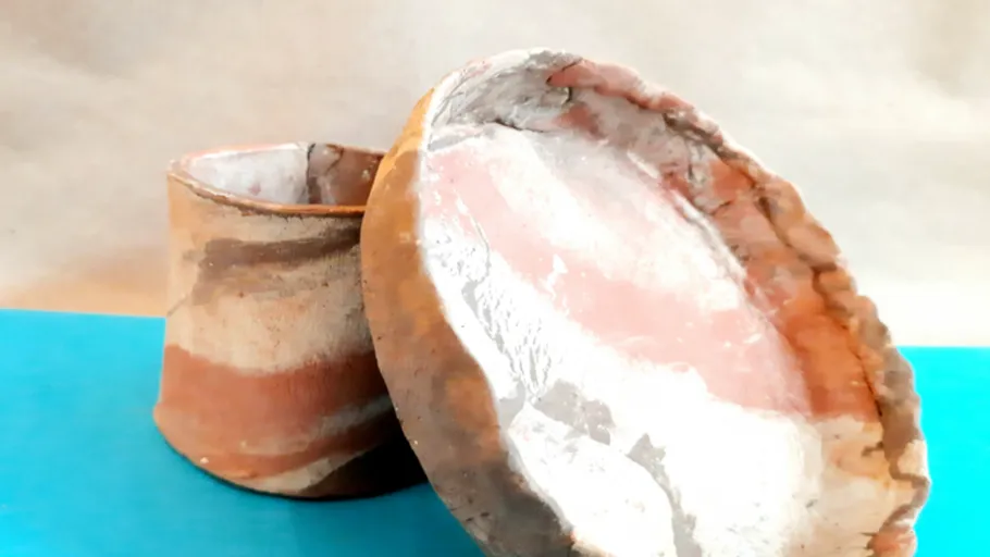 Two handmade clay pots on a blue surface.