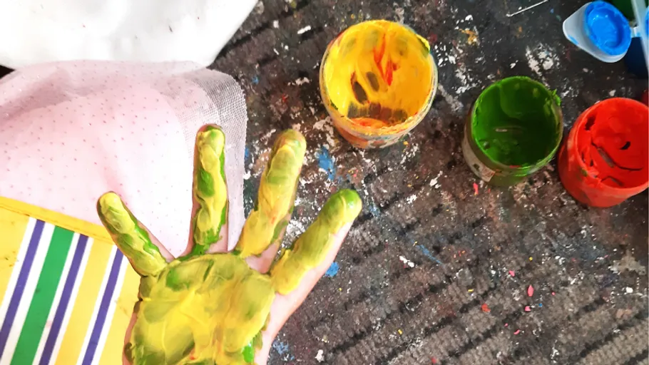Paint-covered hand with colorful pots nearby.