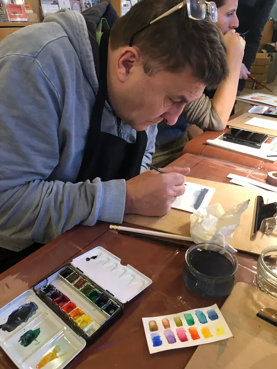 Mann malt mit Wasserfarben an einem Tisch.