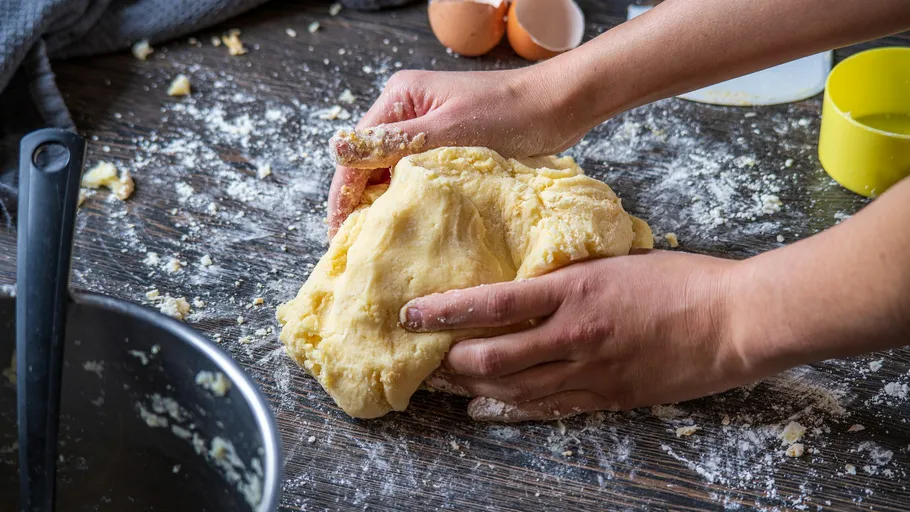 Hands kneading dough on floured wooden table.