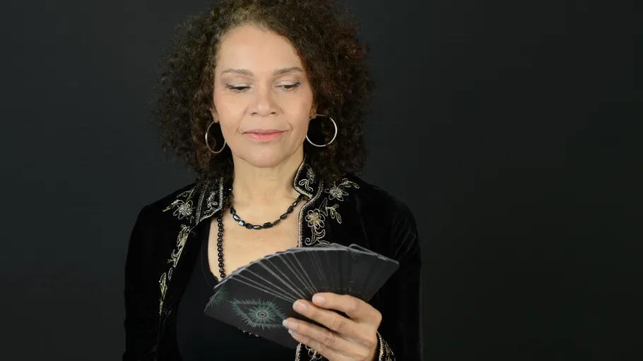 Woman holding tarot cards, black background.