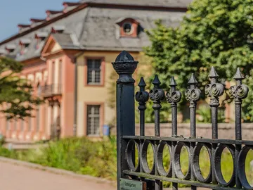 Eisenzaun steht vor einem historischen Gebäude in einem Garten.