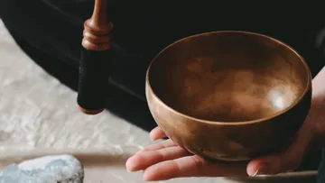 Hand hält eine Klangschale, Klöppel daneben.