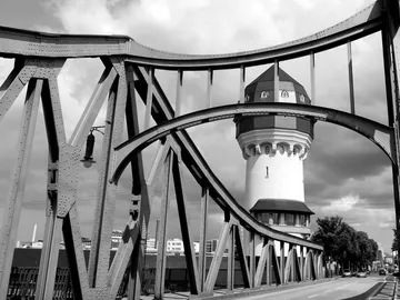 Eisenbrücke umschließt einen historischen Wasserturm in Graustufen.