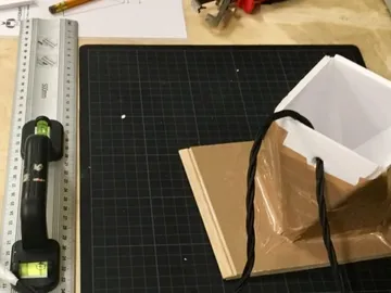 Ein quadratisches Objekt steht auf einem Tisch, umgeben von Werkzeug.
