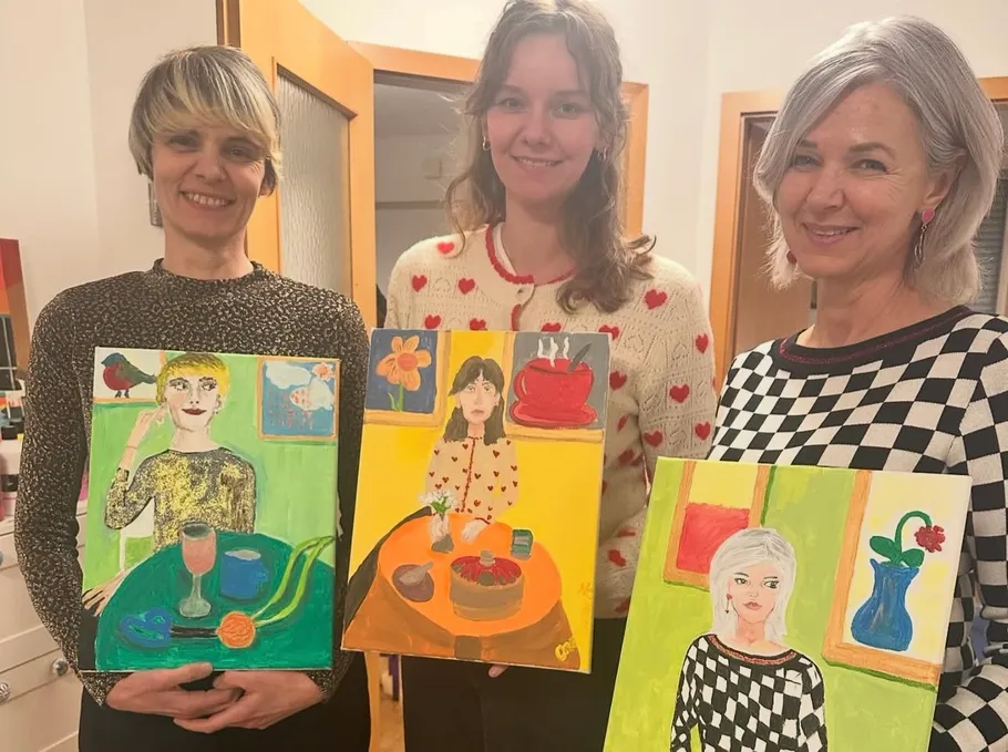 Three women holding colorful paintings indoors.