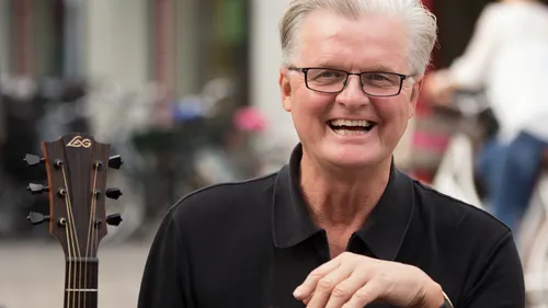 Smiling man with guitar in urban setting.