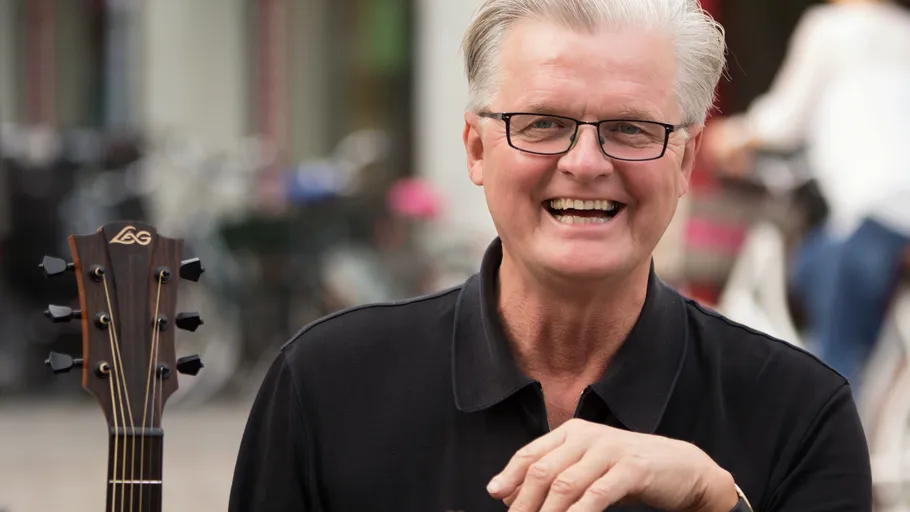 Smiling man with guitar in urban setting.
