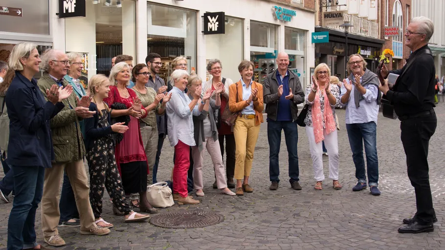 Group clapping for musician on cobblestone street.