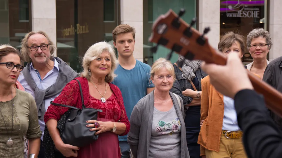 Group watches street performer with guitar outdoors.