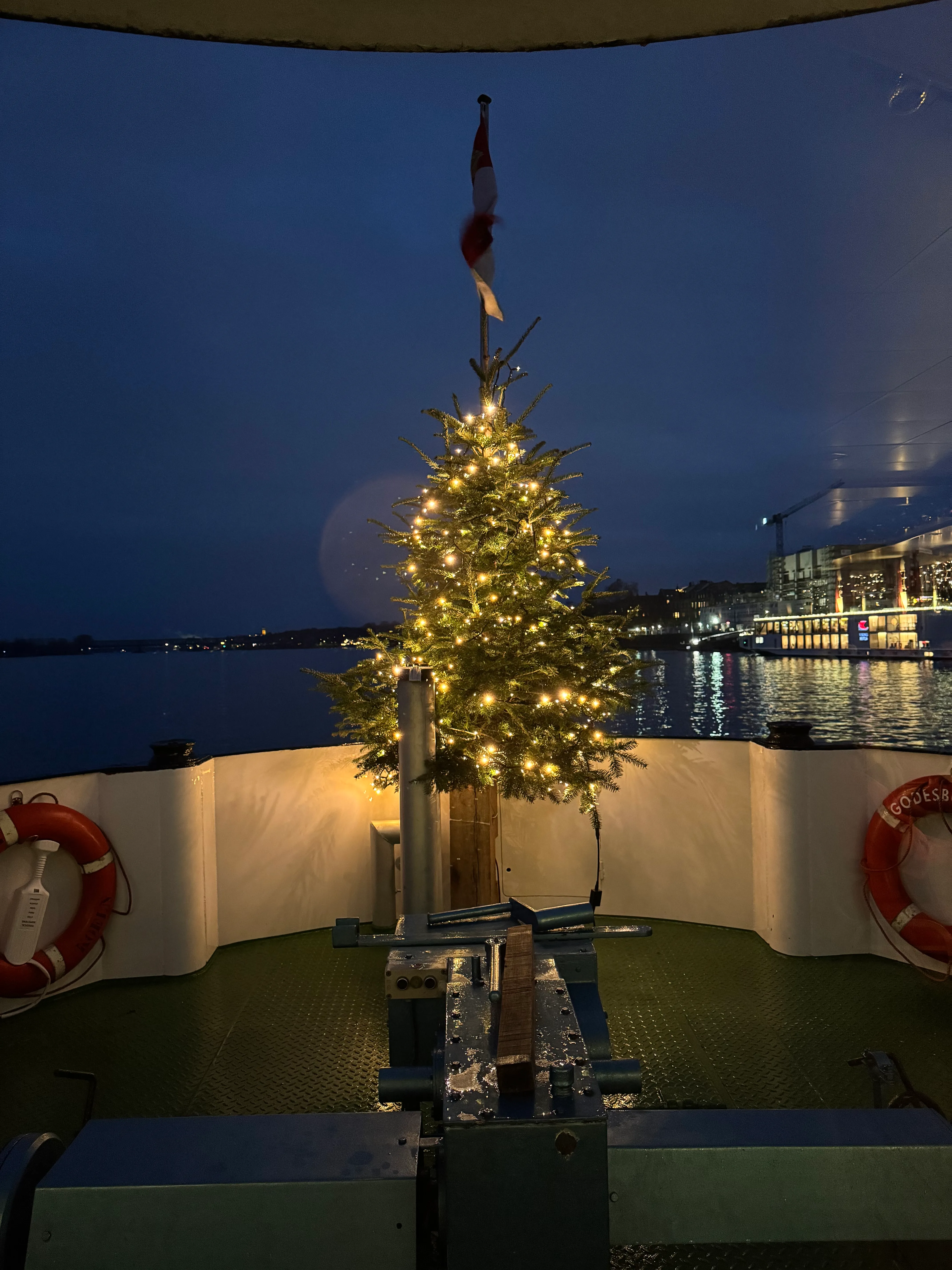 Geschmückter Weihnachtsbaum auf Bootsdeck nachts.