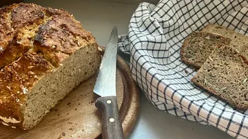 Laib Brot und Scheiben mit Messer auf Tisch.