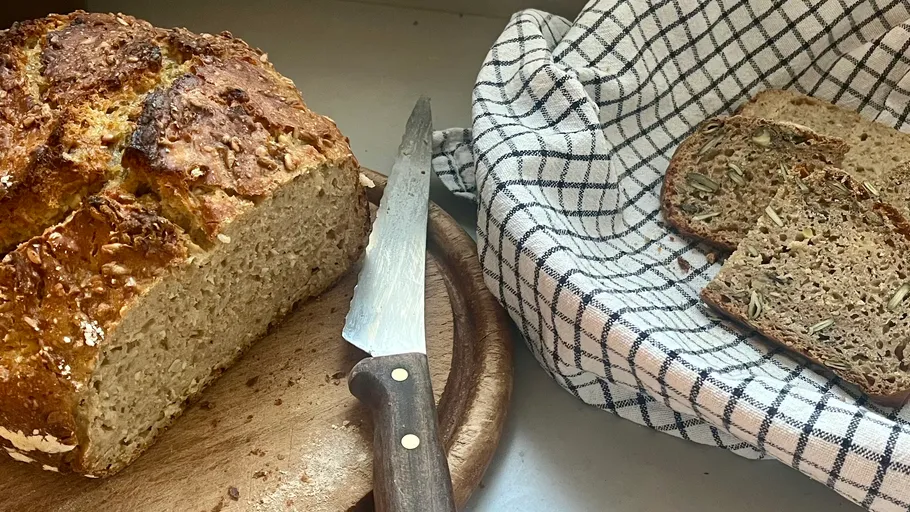 Loaf of bread and slices with knife on table.