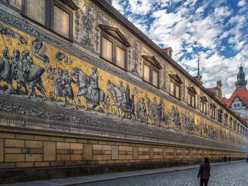 Wandmalerei zeigt historische Szenen; Menschen gehen vorbei.