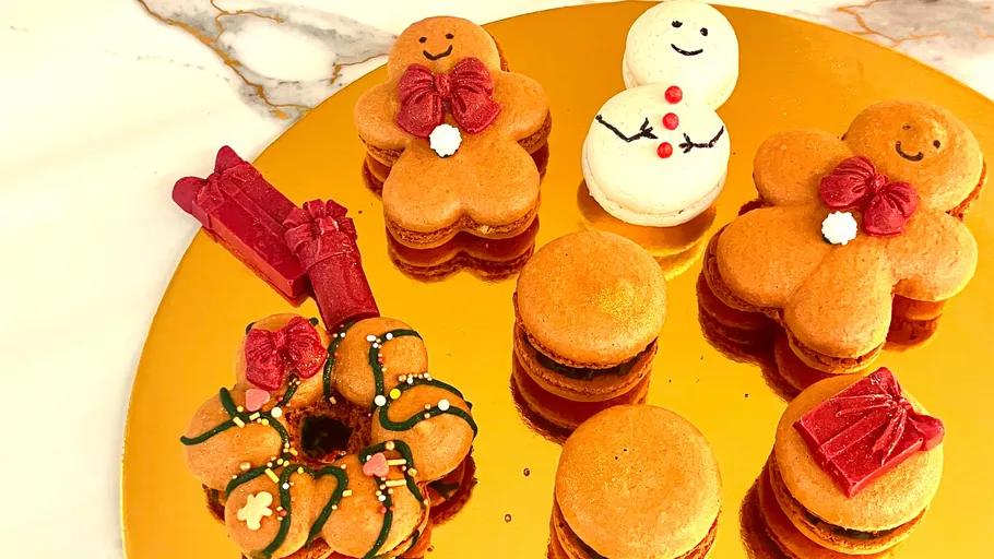 Festive macarons shaped like snowmen and gingerbread on tray.