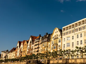 Bunte Gebäude stehen am Fluss unter blauem Himmel.