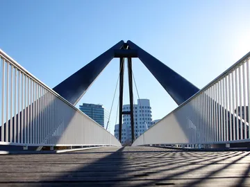 Hängebrücke verbindet zwei Ufer, umgeben von modernen Gebäuden.