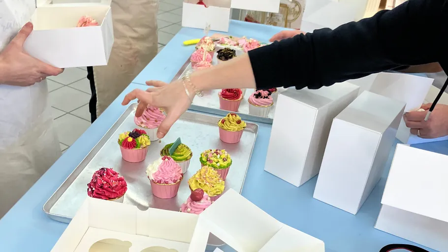 Hands packing colorful cupcakes into boxes.