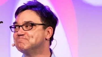 Person with glasses speaking on stage.
