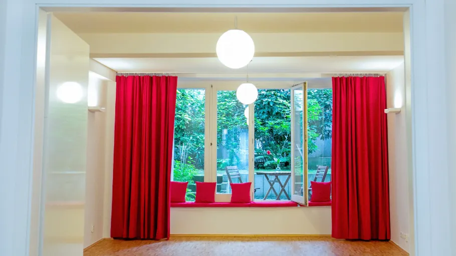Room with red curtains overlooking garden.