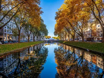 Ein Kanal spiegelt bunte Herbstbäume und Gebäude wider.
