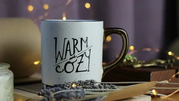Mug with 'Warm and Cozy' text, fairy lights behind.