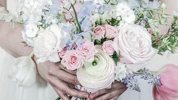 Hands holding bouquet with pastel flowers.