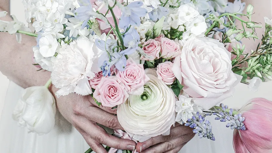 Hände halten Strauß mit pastellfarbenen Blumen.