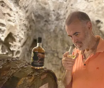 Man smelling drink beside barrel in cellar.