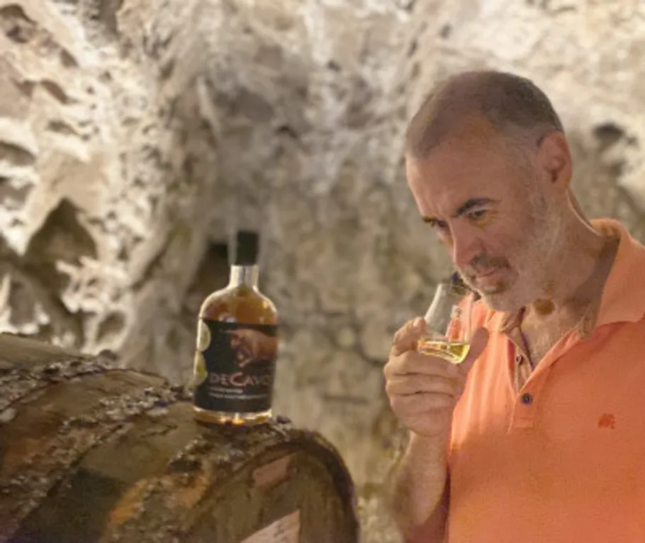 Man smelling drink beside barrel in cellar.