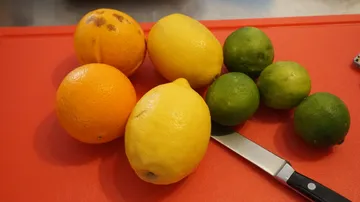 Zitrusfrüchte und Messer auf rotem Schneidebrett.