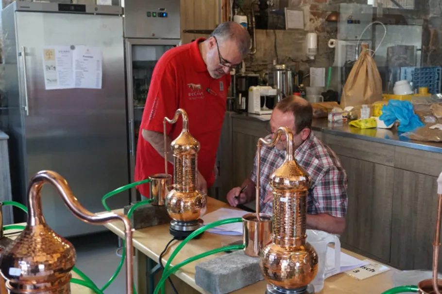 Two men work with copper distillation equipment.