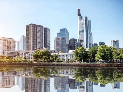 Skyscrapers reflect in the calm water of a river.