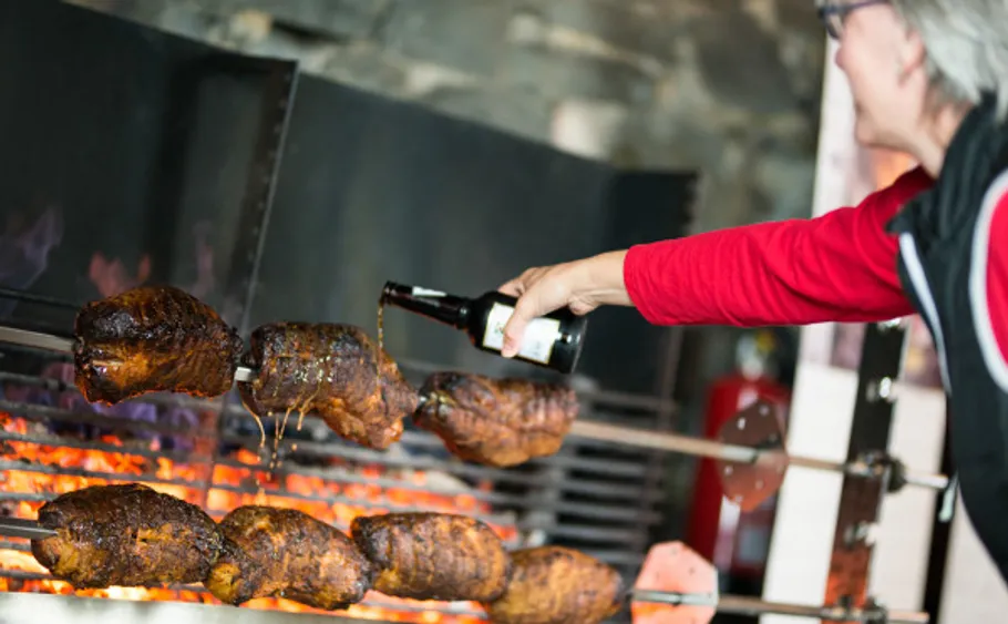 Person pouring liquid on roasting meat outdoors.