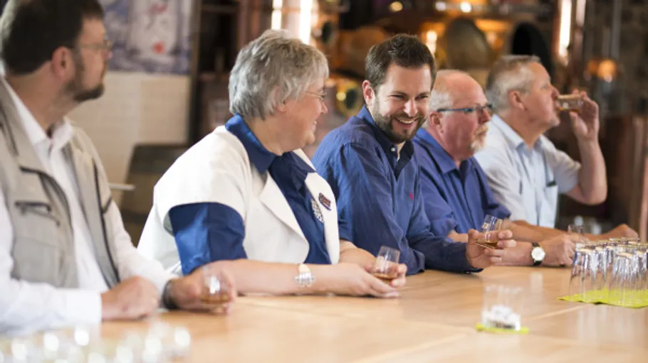 Group tasting whiskey at a distillery table.