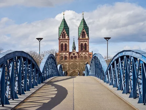 Blue bridge leads to a church under a cloudy sky.