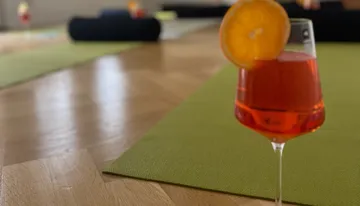 Orange cocktail on yoga mat, wooden floor.